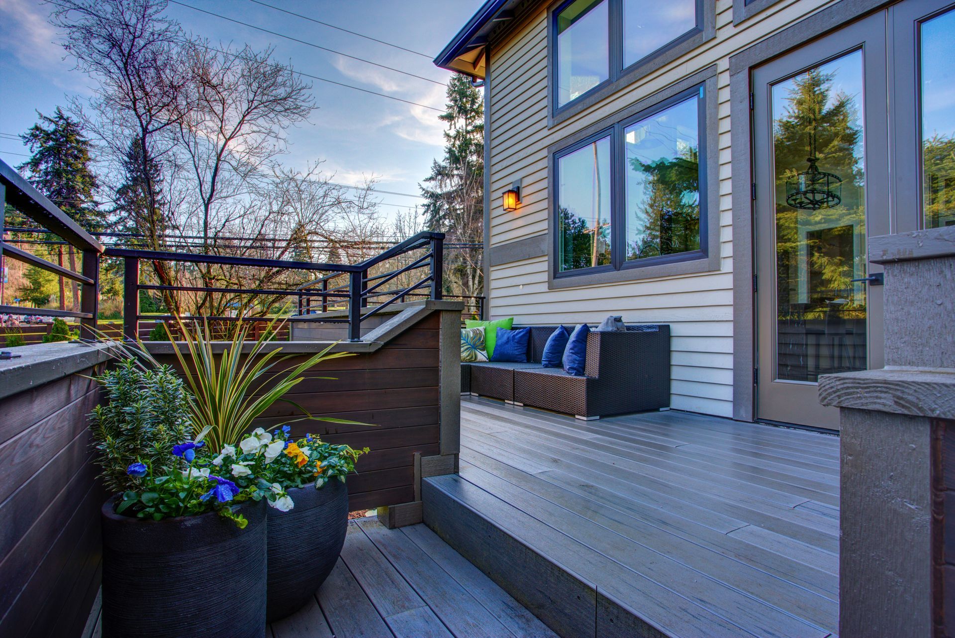 Outdoor deck with potted plants, seating, and a modern house.