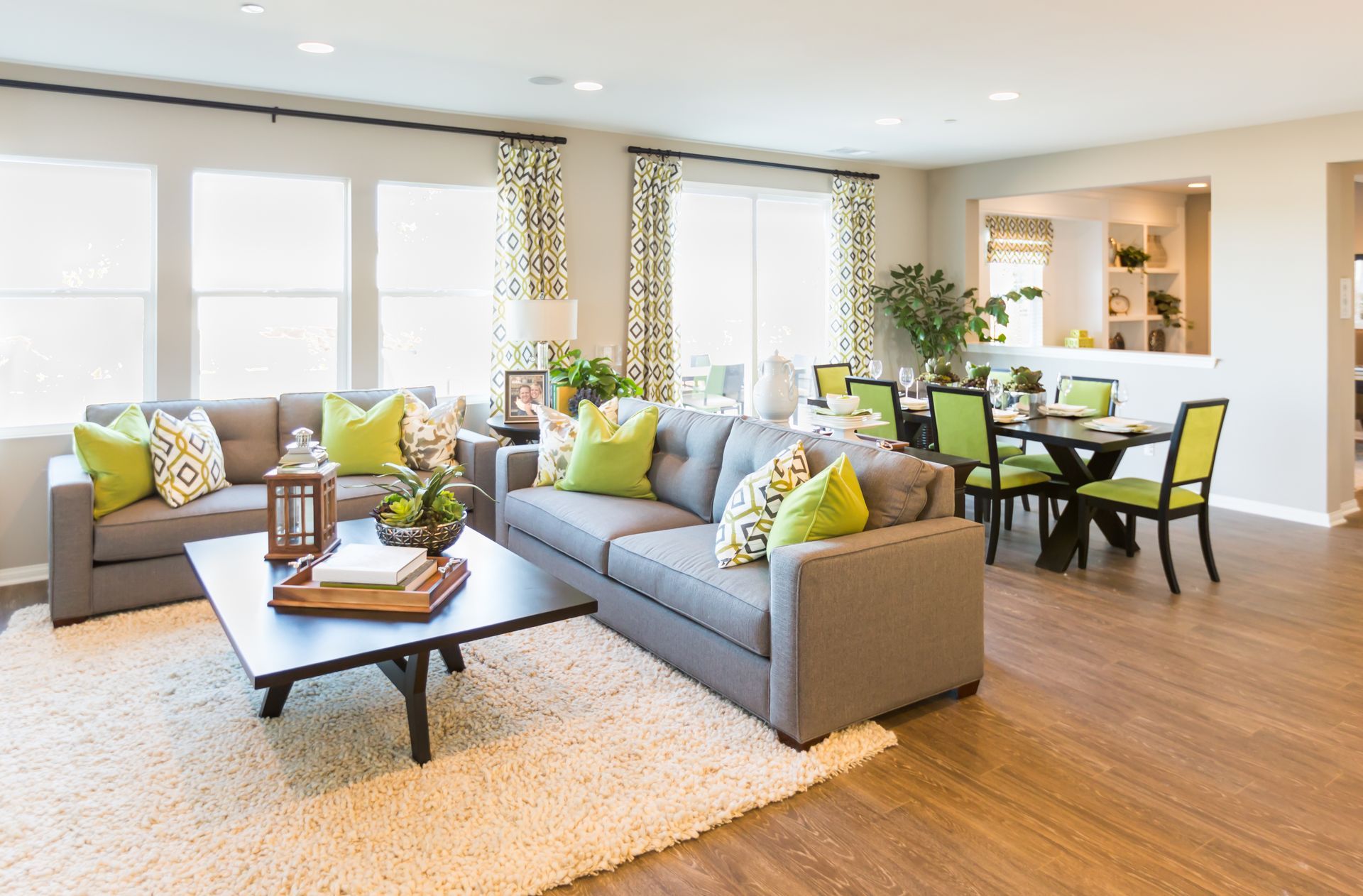 Living room with grey sofas, green pillows, wooden floors, and dining area.