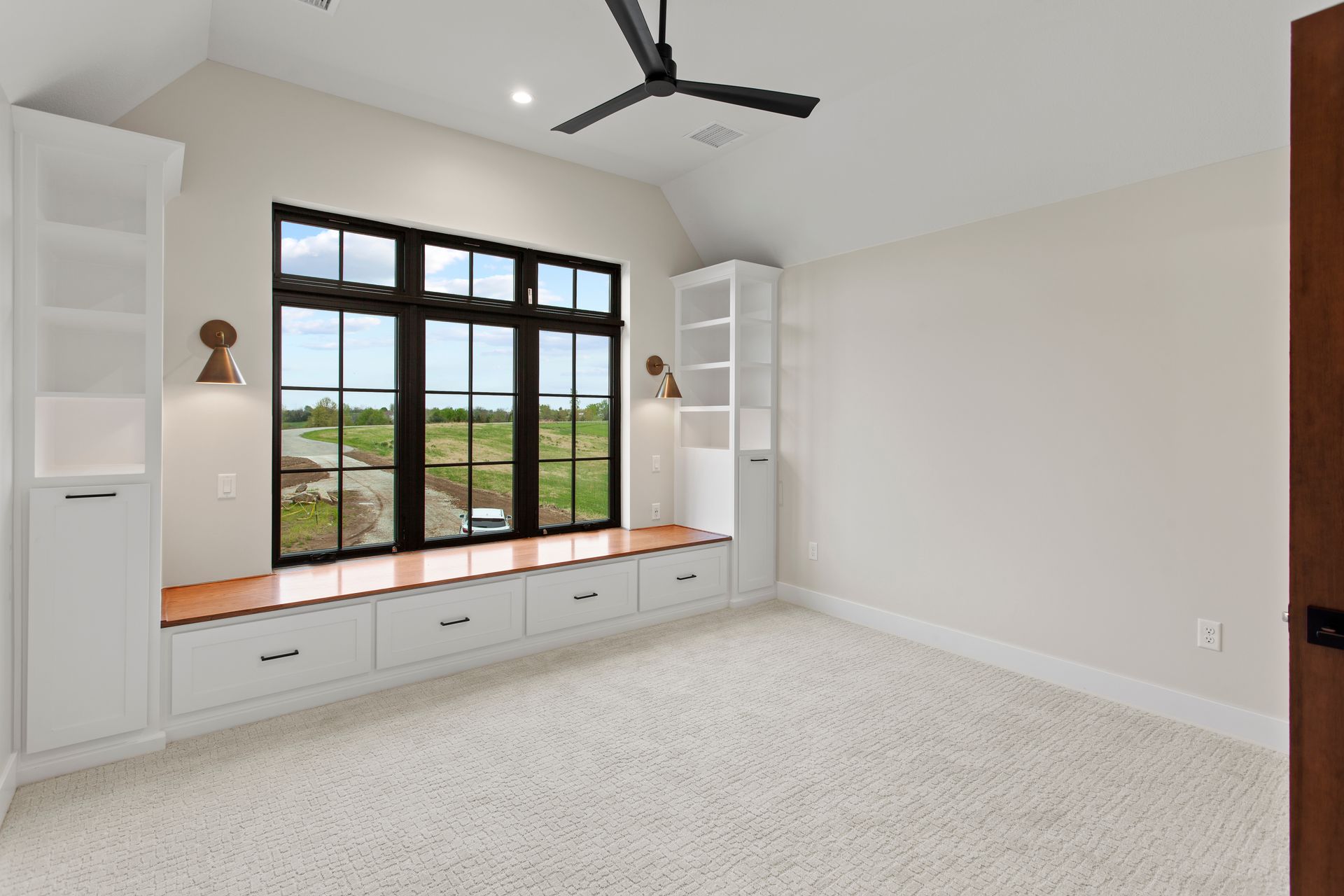 Bedroom with large window, built-in storage, and a light-colored carpet, overlooking a green field.