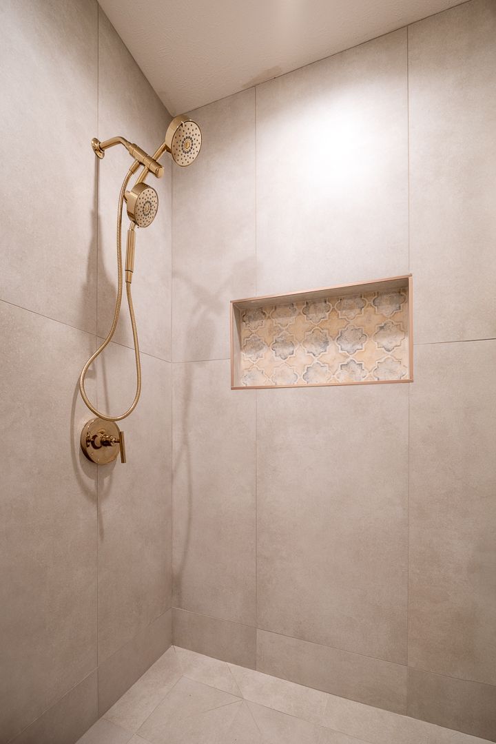 Shower with gold fixtures and built-in niche in a minimalist, tiled bathroom.