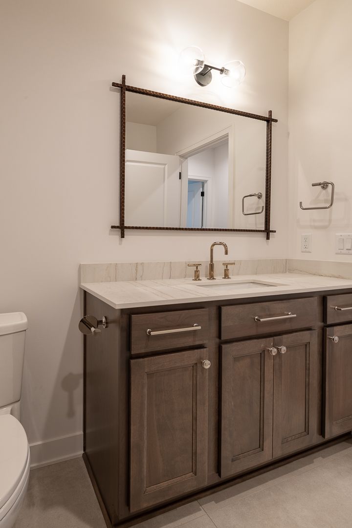 Bathroom with brown vanity, rectangular mirror, white countertop, and silver fixtures.