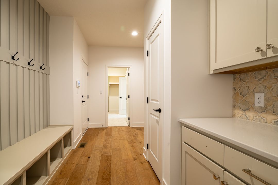 Hallway with wooden floor, bench, hooks, and cabinets. Bright white walls and natural light.