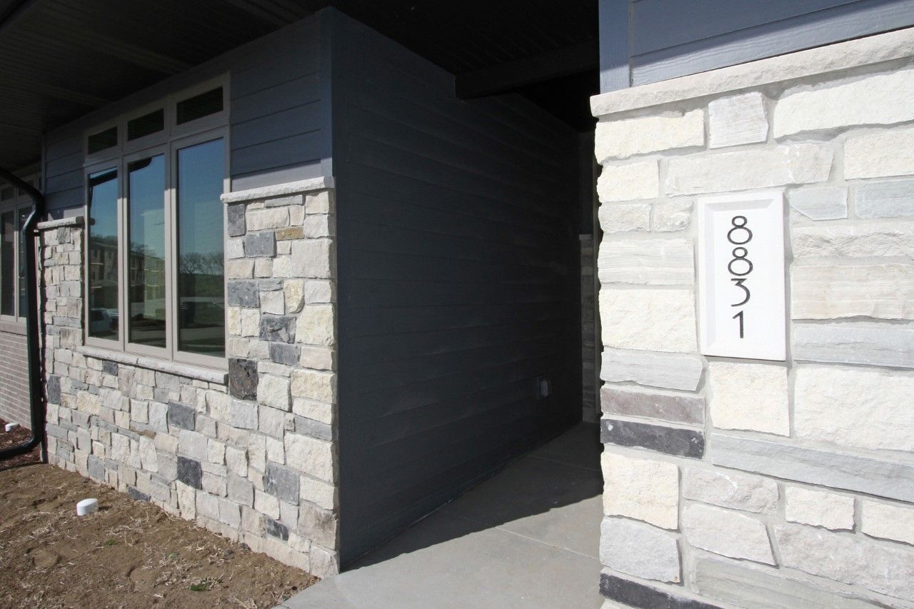 Exterior of a house with stone and dark siding. The house number
