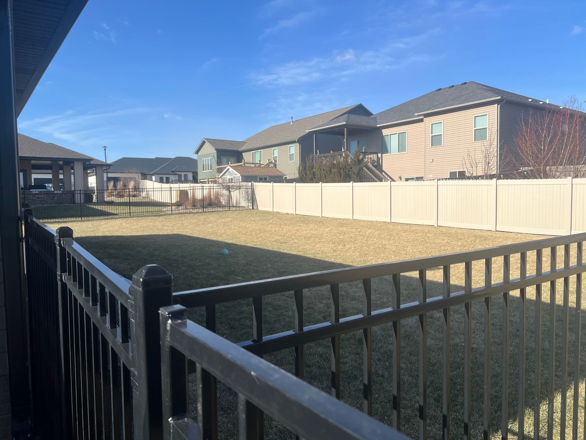 Backyard view with fence, grass, houses, and a clear blue sky.