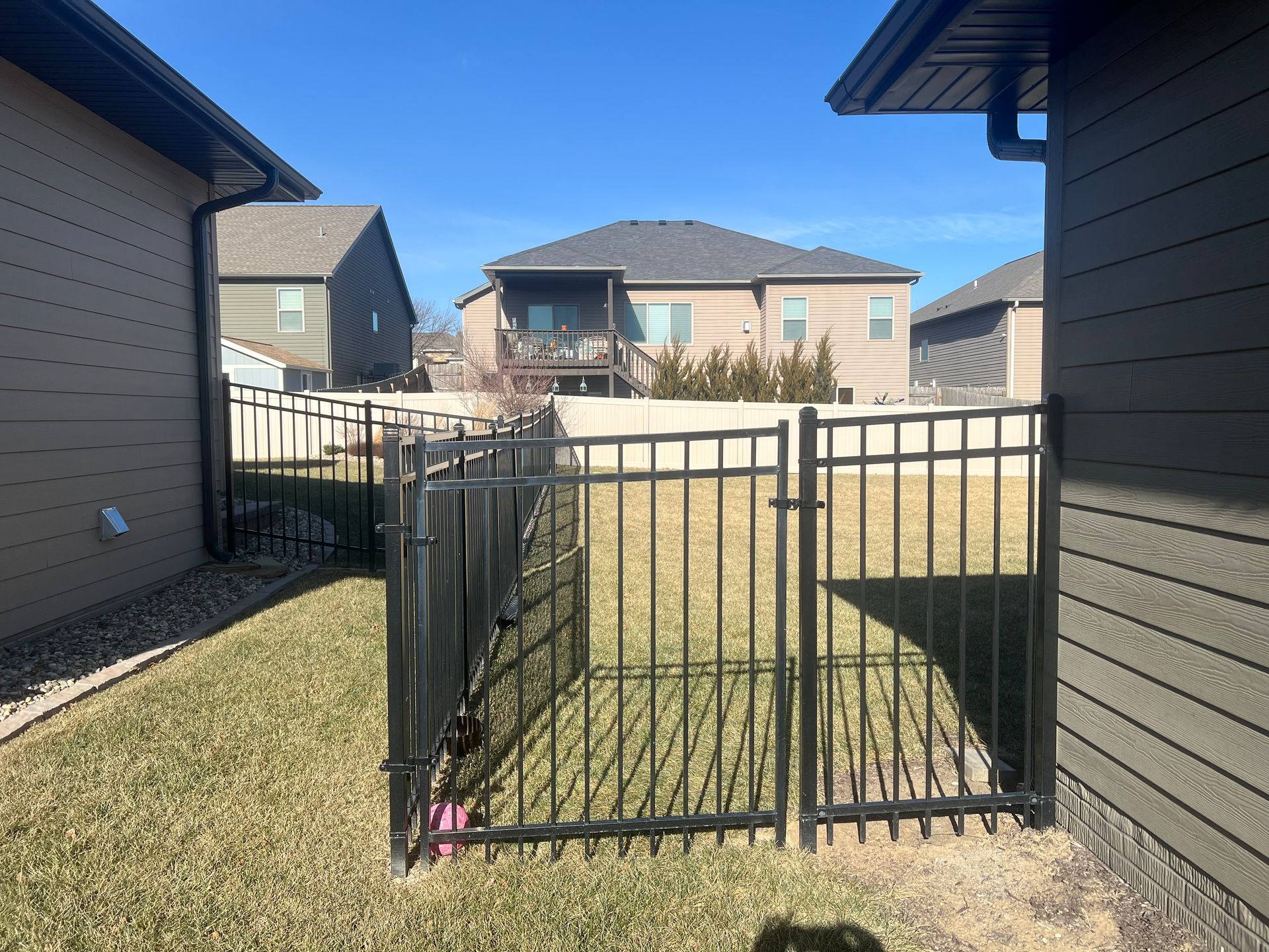 Black metal fence between two houses, gate open to backyard with other houses in the distance.