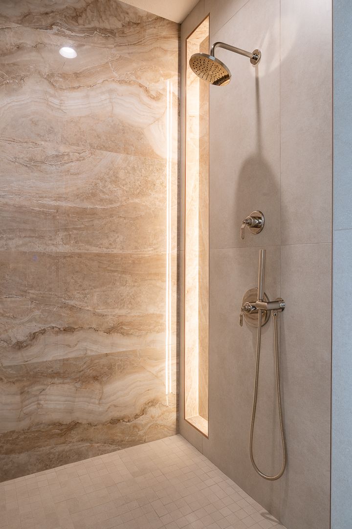Shower with beige and tan stone walls, chrome fixtures, and a handheld showerhead.