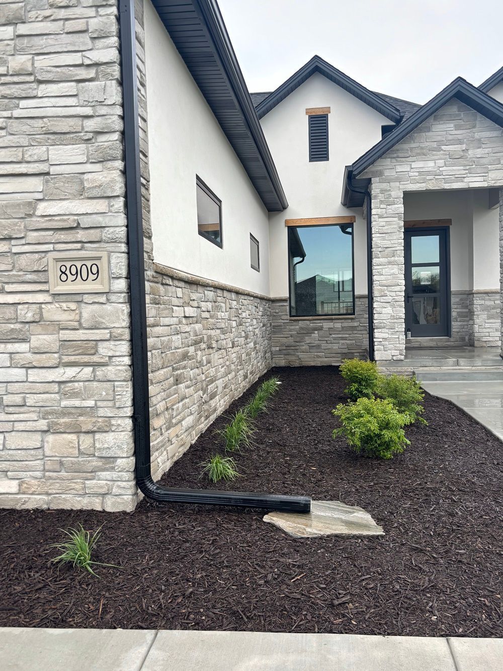 Exterior view of a house with stone and white siding, black downspout, and landscaped front yard with mulch.