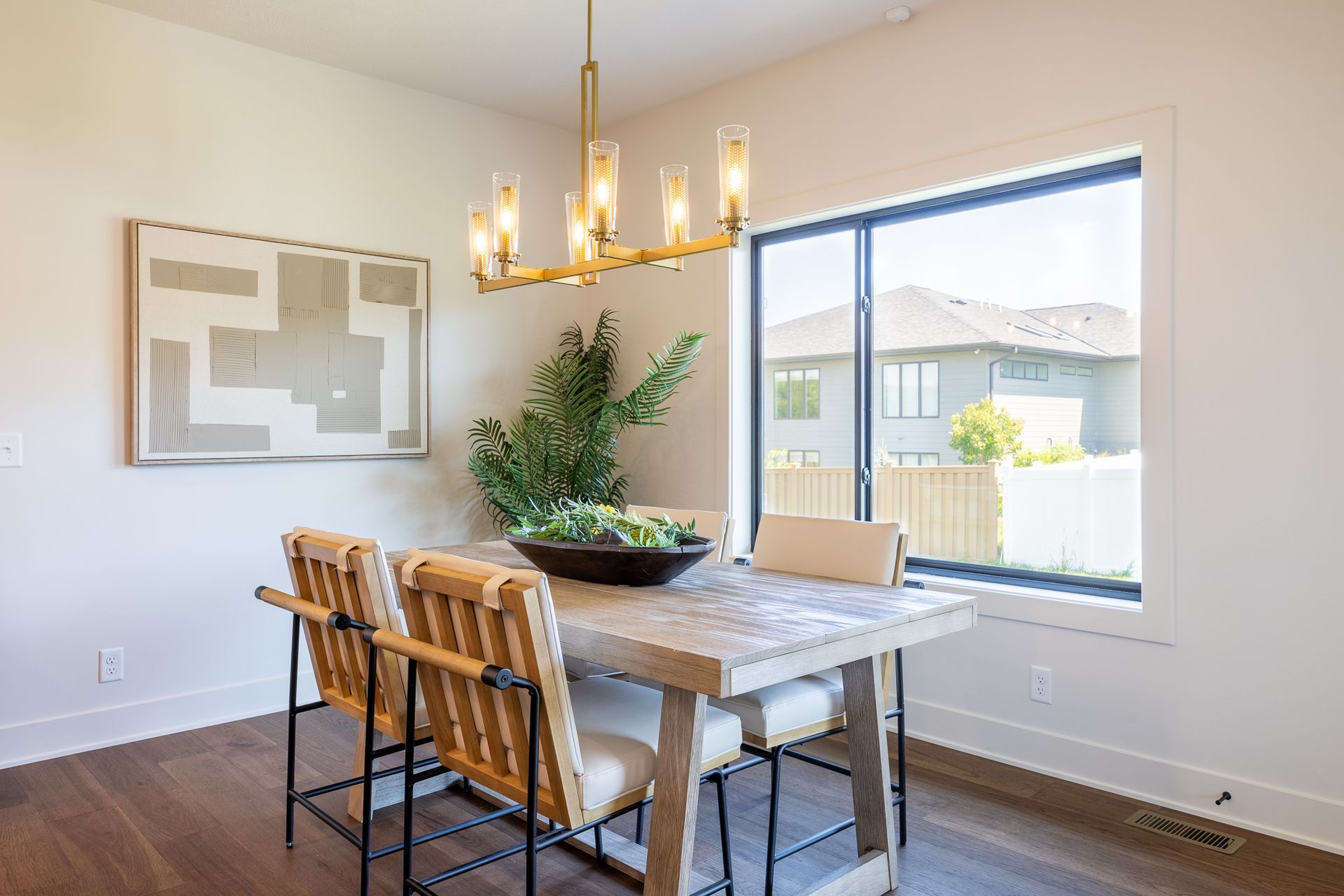 Dining room with a wooden table, chairs, art, window, and gold chandelier.