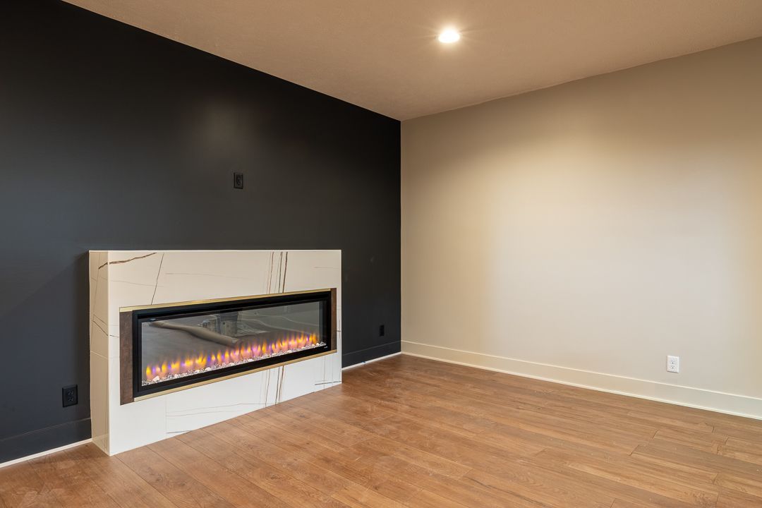 Empty room with a fireplace, black accent wall, and wood flooring.