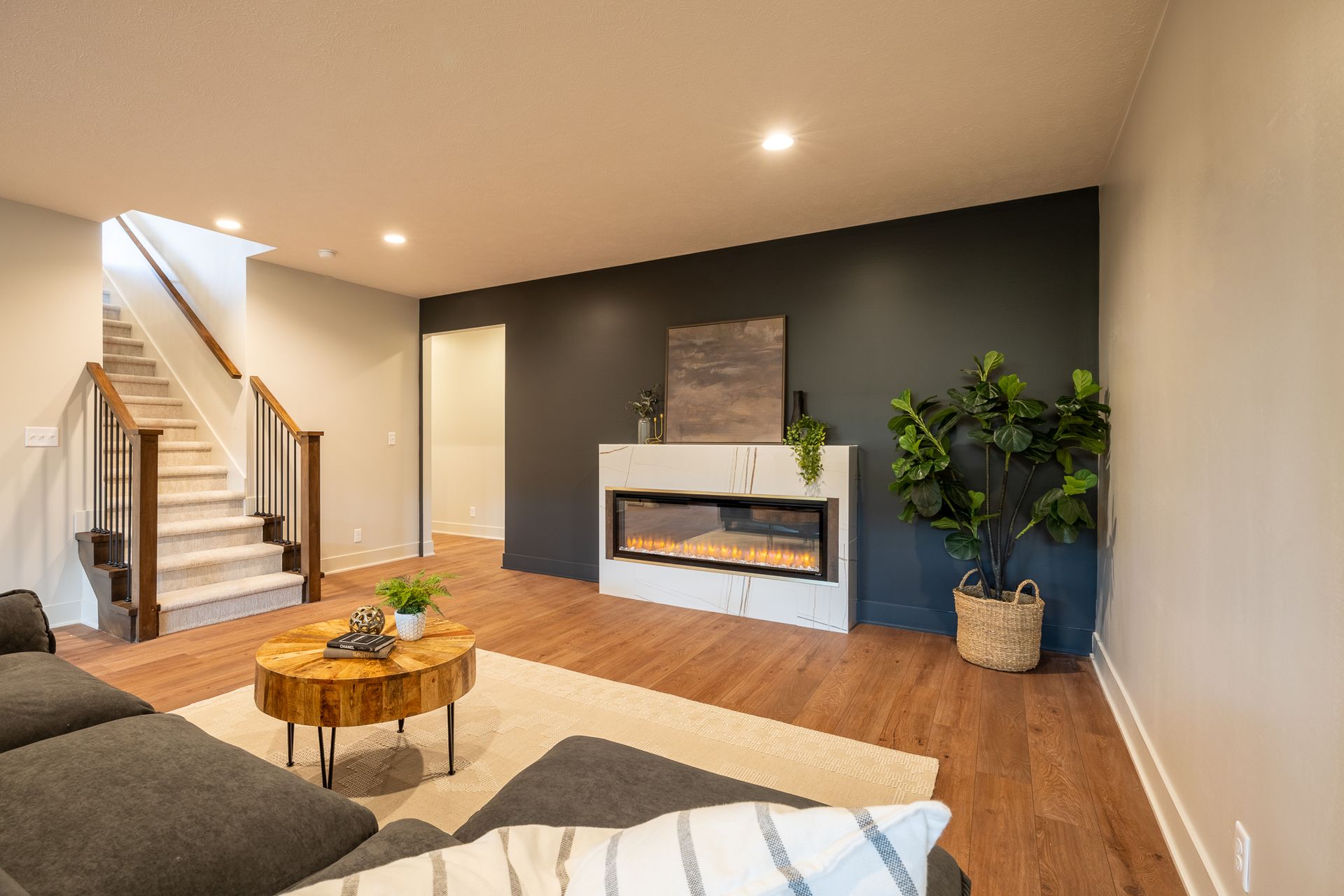 Living room with wooden floors, fireplace, and staircase. Dark accent wall, neutral paint, modern decor.
