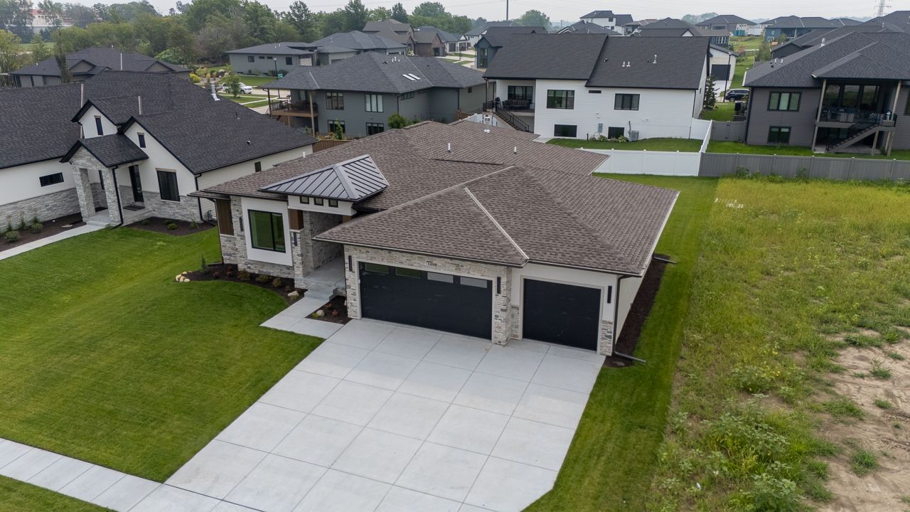 Modern house with dark roof and gray garage doors. Concrete driveway and green lawn.
