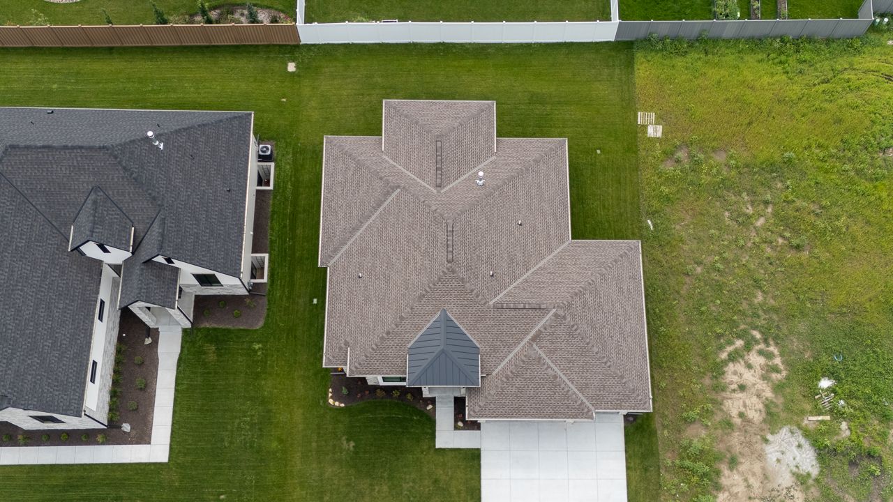Aerial view of a house with a complex roof and attached driveway, surrounded by green grass.