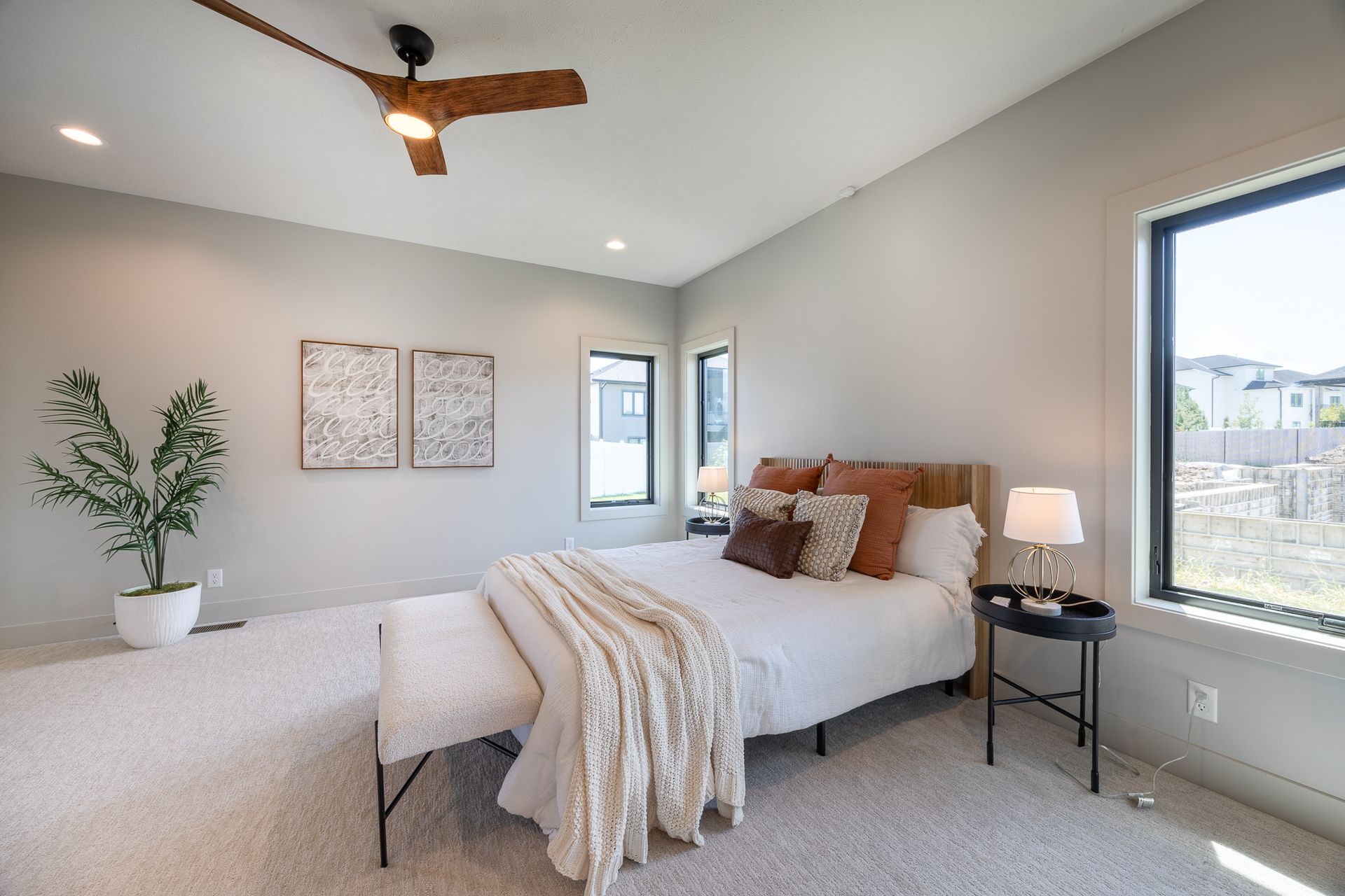 Bedroom with bed, pillows, blanket, side table, windows, and ceiling fan.