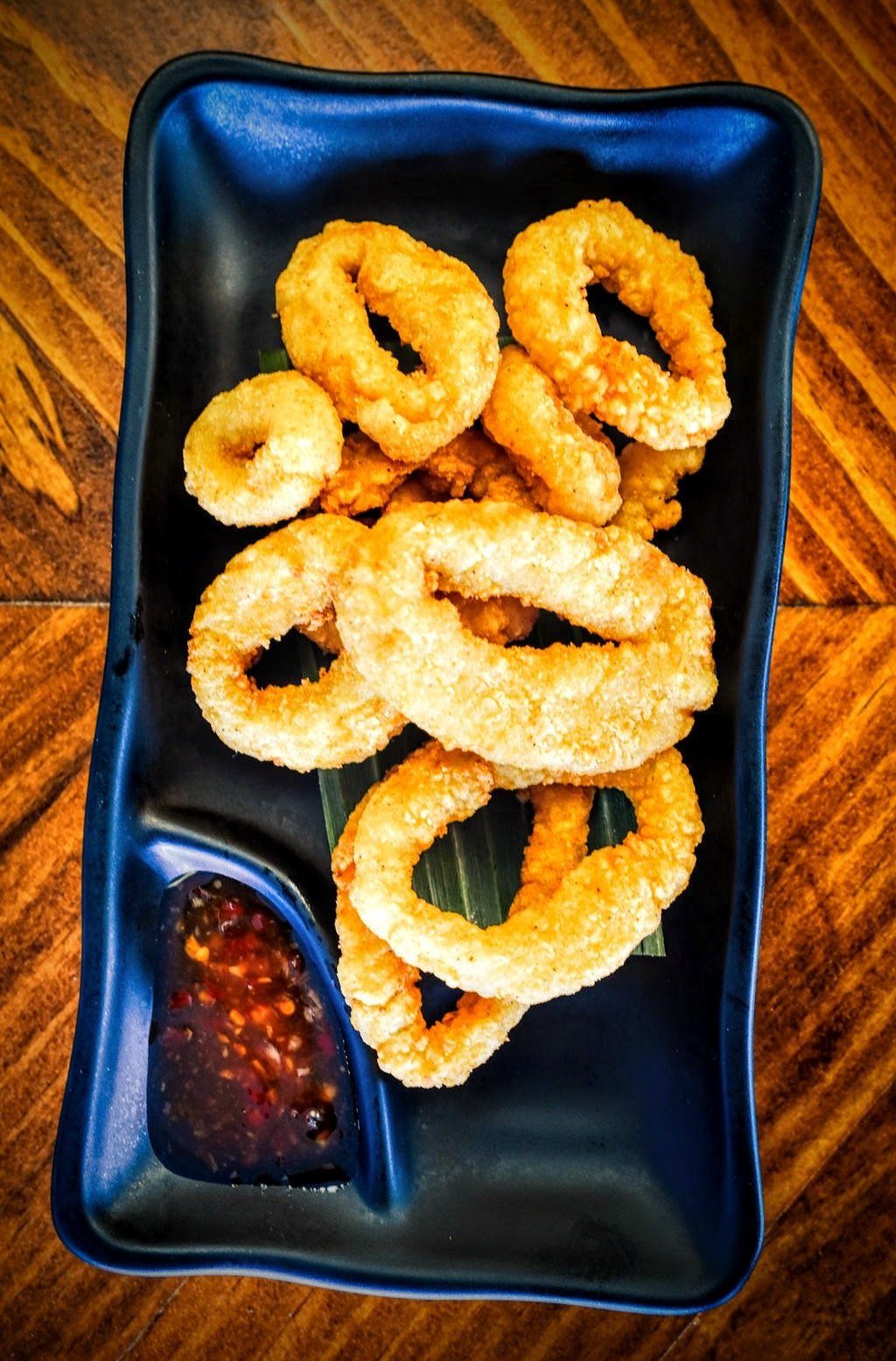 a black plate topped with fried onion rings and dipping sauce on a wooden table .