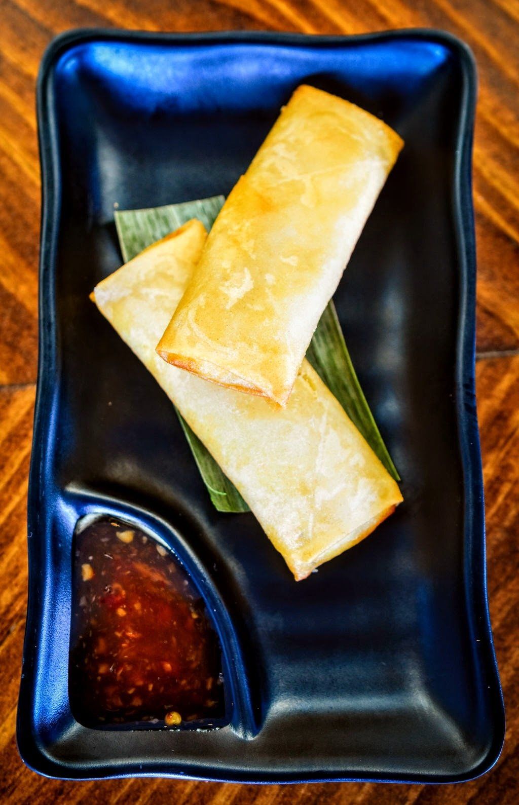 two egg rolls are on a black plate with dipping sauce .