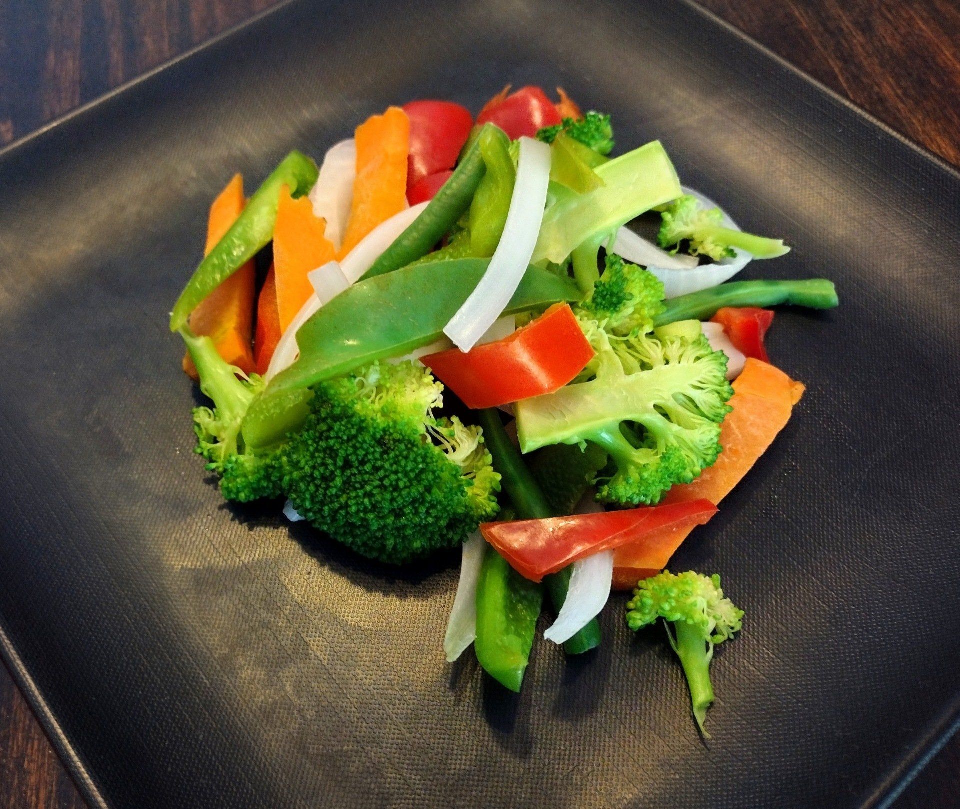 a black plate topped with broccoli carrots peppers and onions