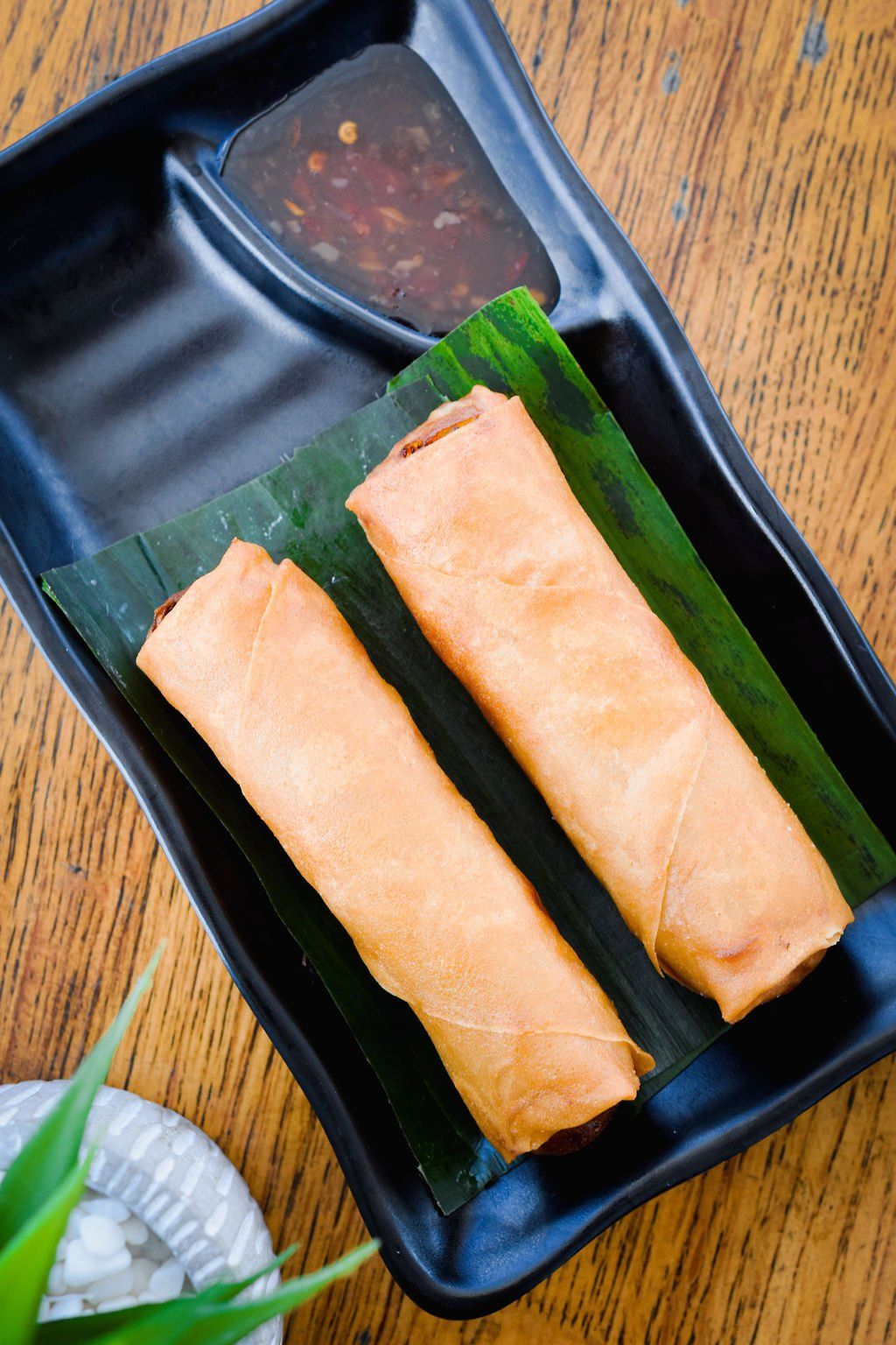 two egg rolls on a black plate with dipping sauce on a wooden table .