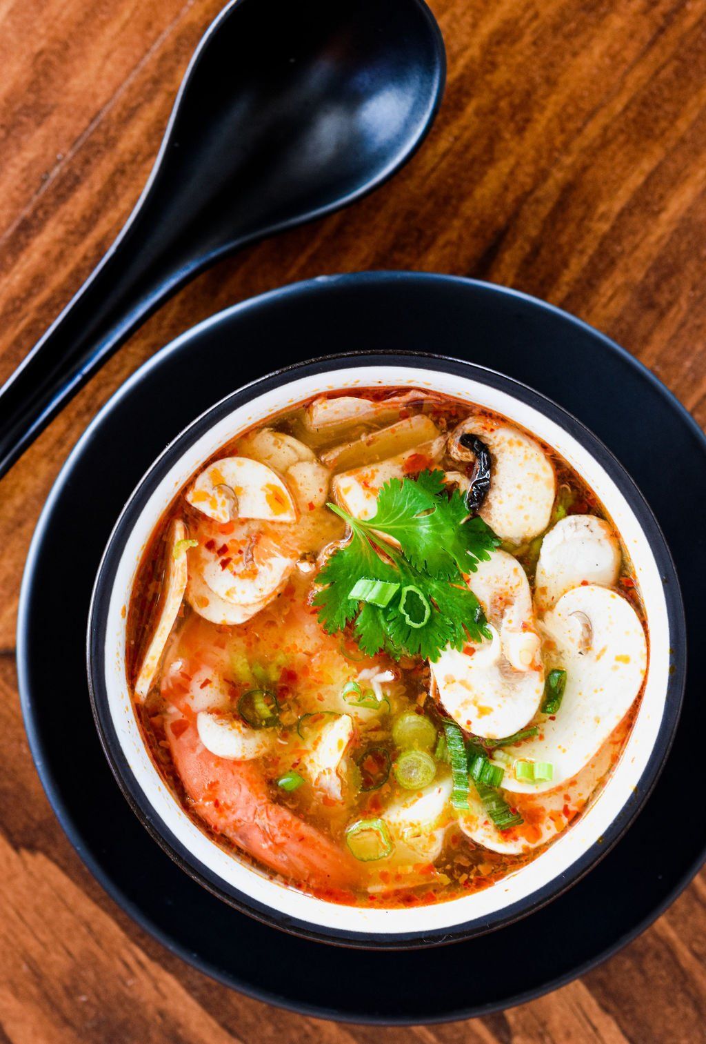 a bowl of shrimp and mushroom soup with a spoon on a wooden table .