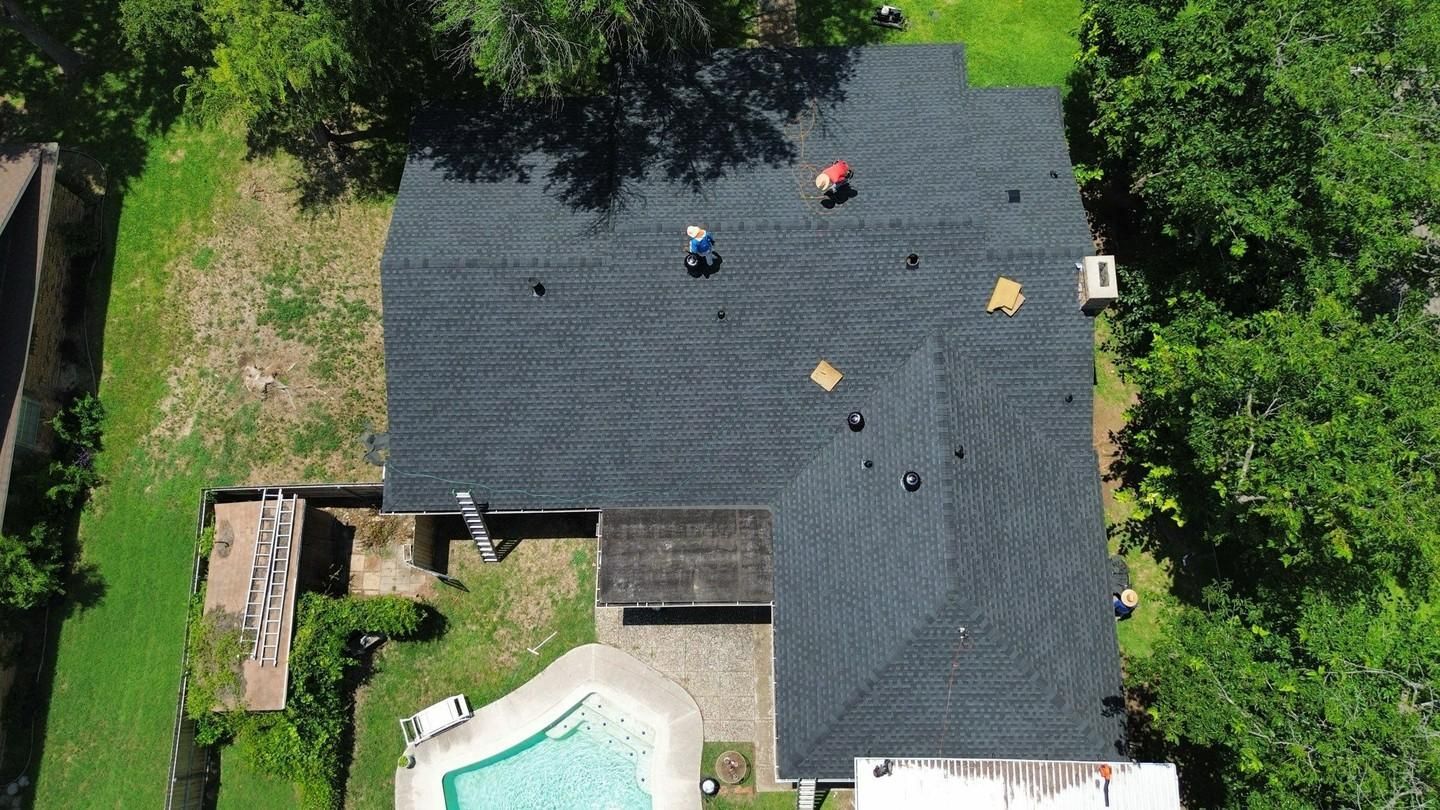 Aerial view of house roof with workers, pool, and surrounding trees.