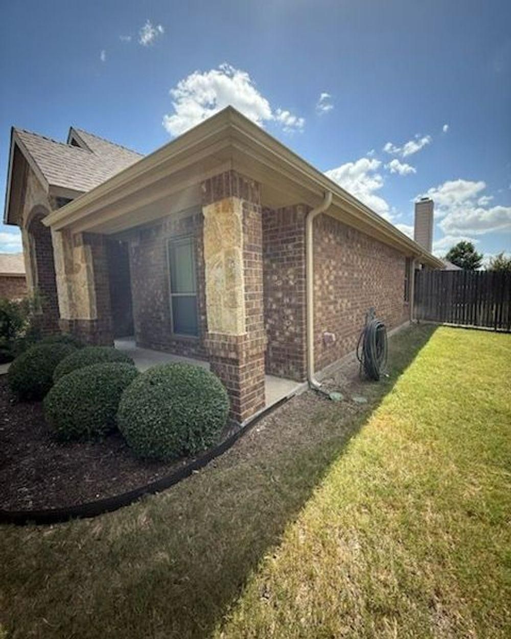 Brick house with green lawn, bushes, and a blue sky.