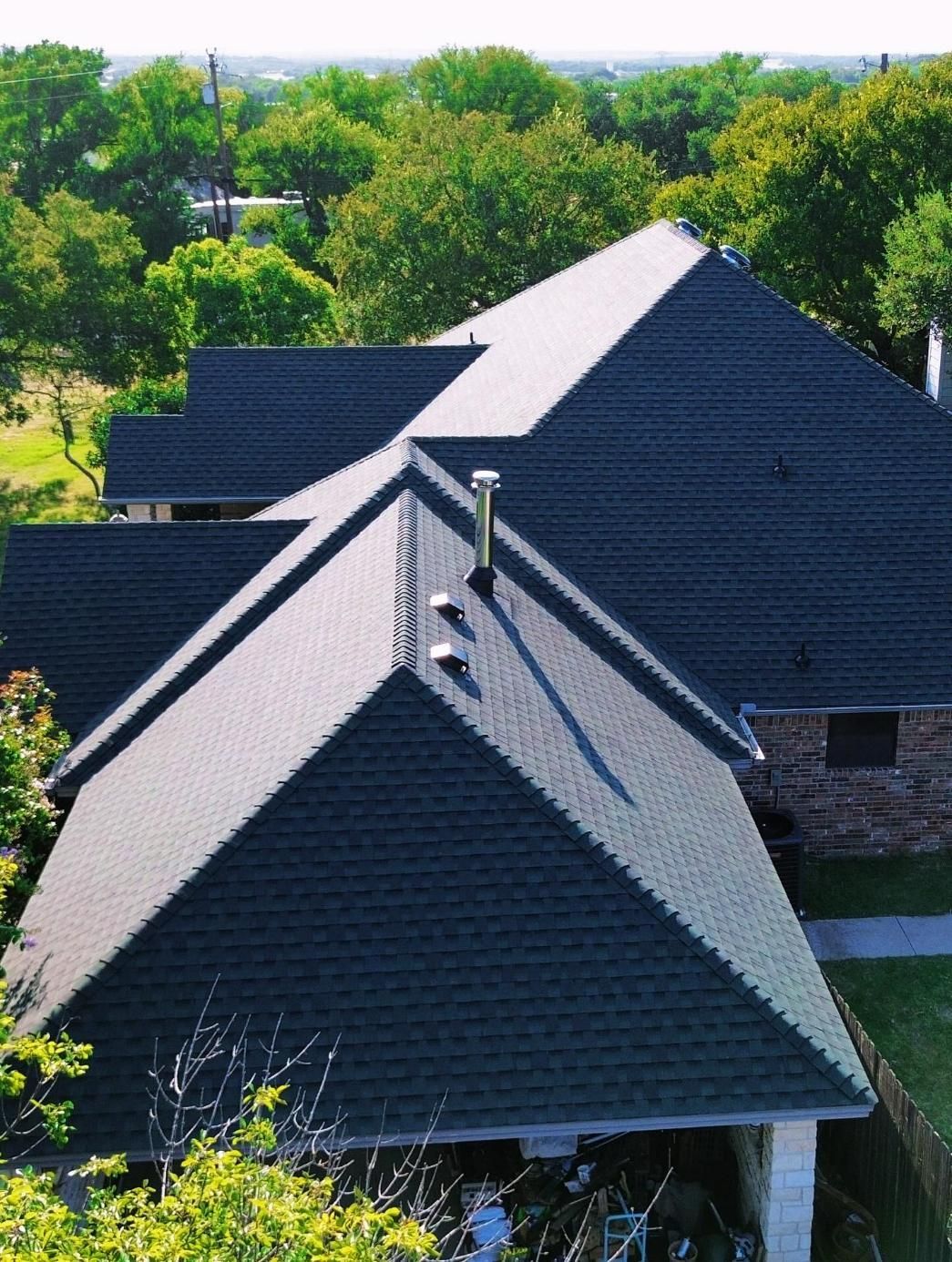Dark green roof on a house, viewed from above, surrounded by green trees.