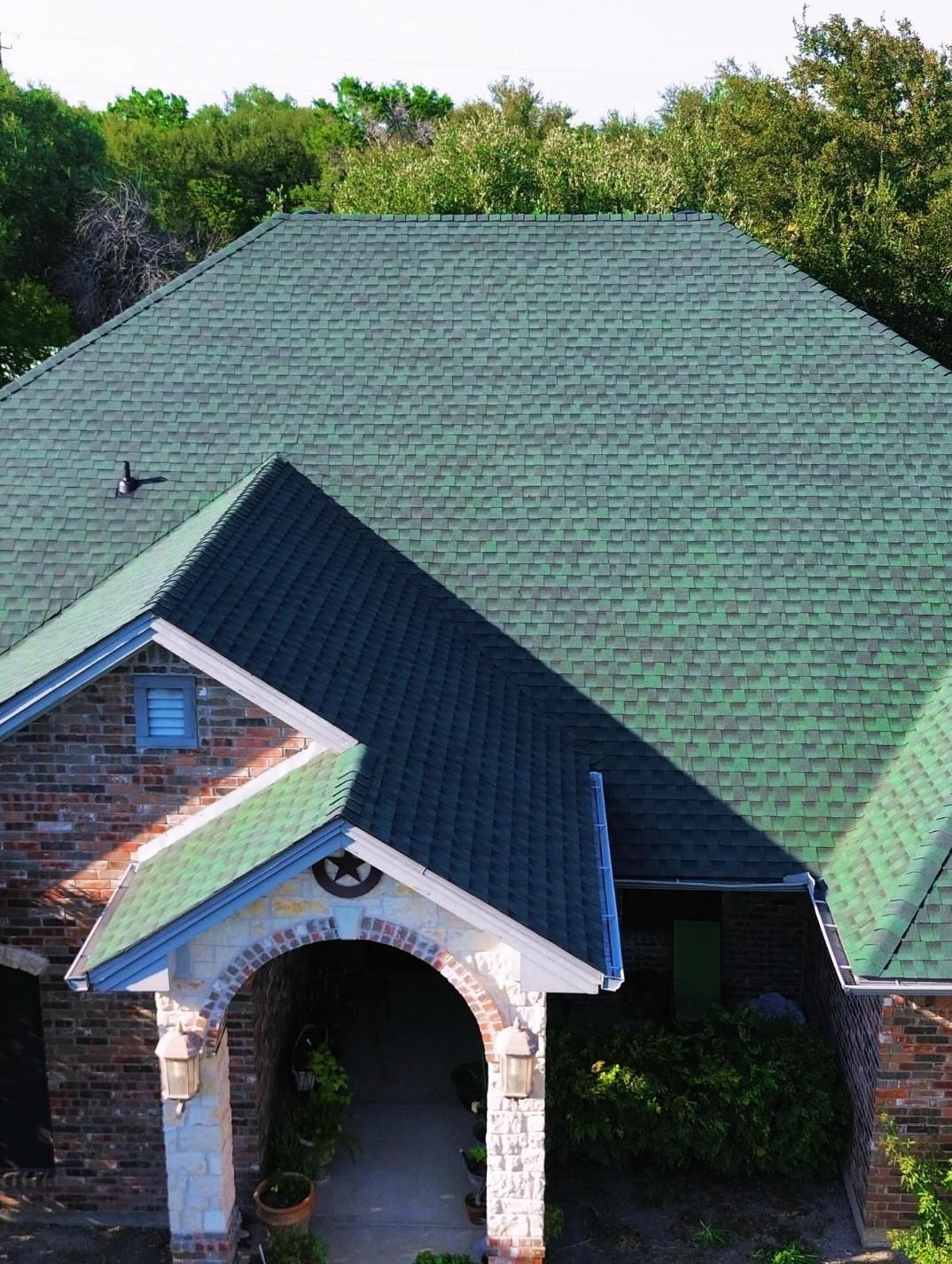 Green shingled roof of a house with brick facade and arched entrance.