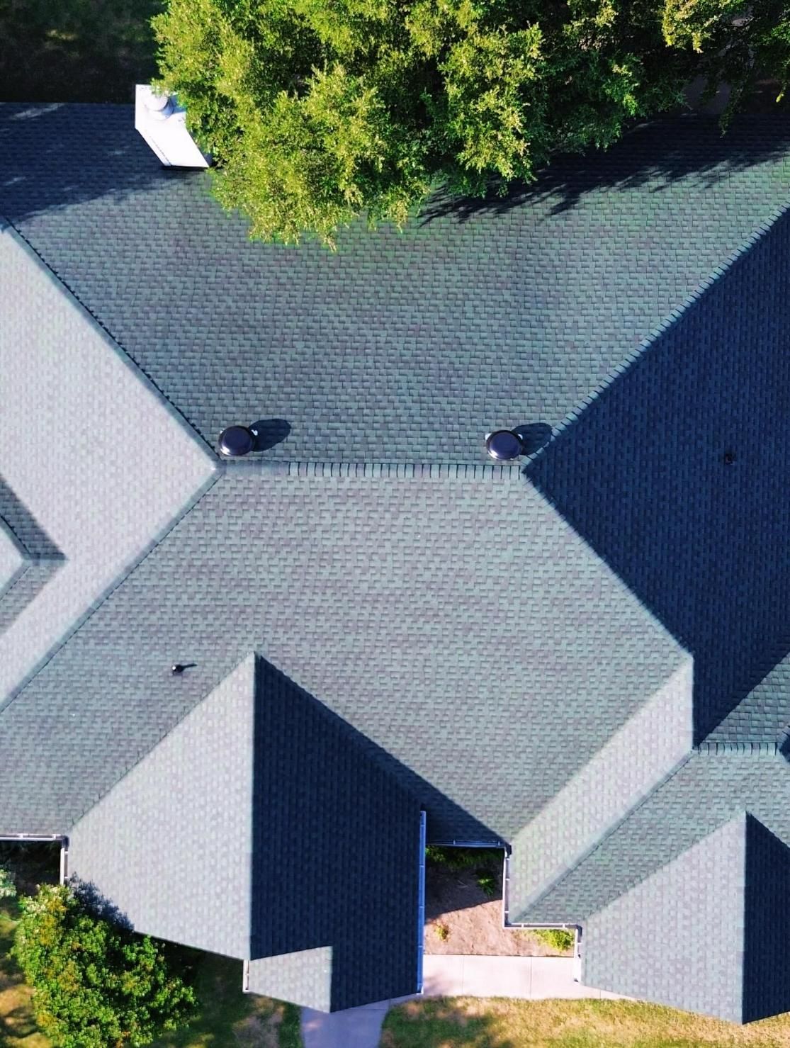 Overhead view of a dark blue shingled roof with a tree and white chimney.