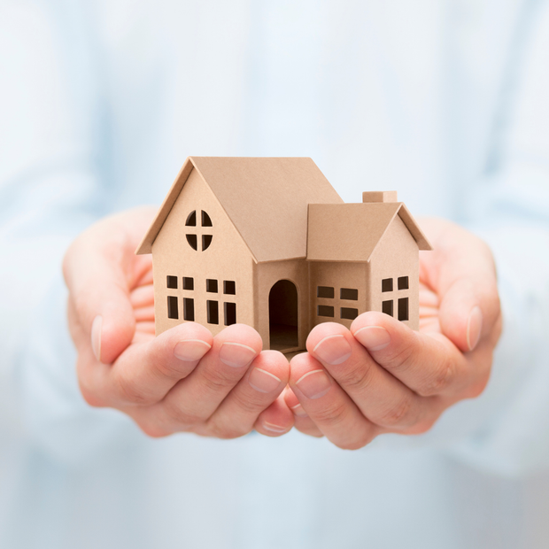 Hands cradling a small cardboard house model, symbolizing real estate or home ownership.