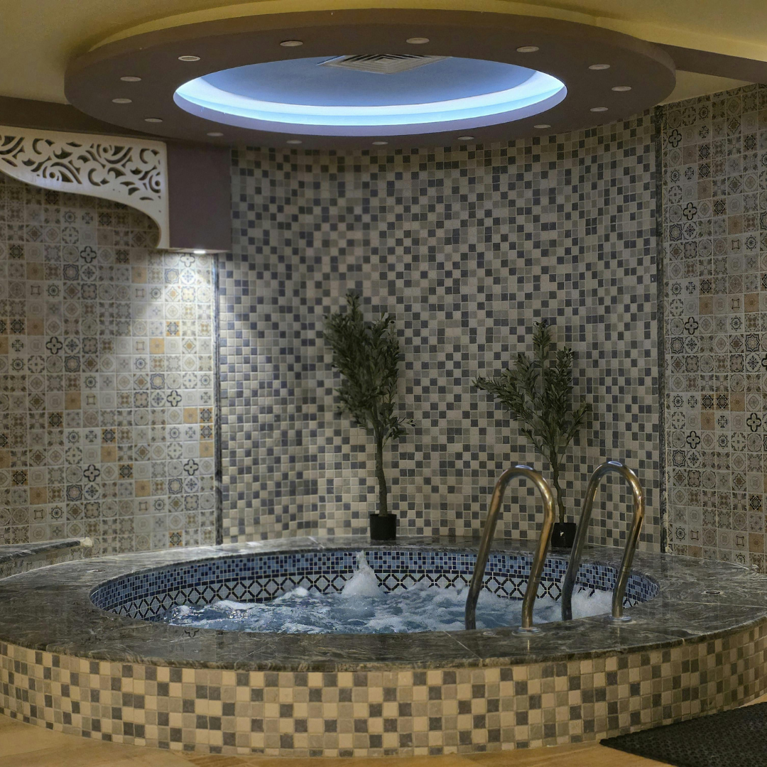 Hot tub with bubbling water, tiled walls, ceiling lighting, and small trees.