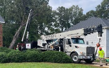 A white truck with a crane attached to it is parked in front of a house.