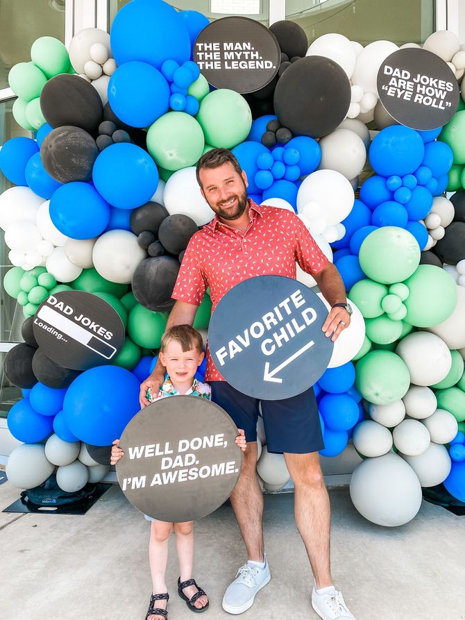 a man and a child are holding signs in front of a wall of balloons
