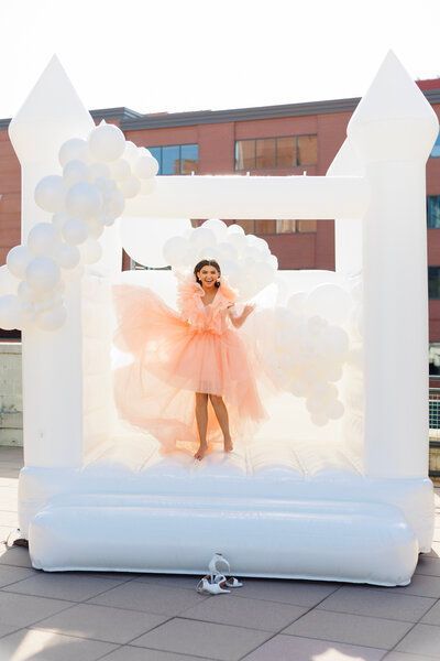 a woman in a pink dress is standing in a white bouncy house surrounded by white balloons
