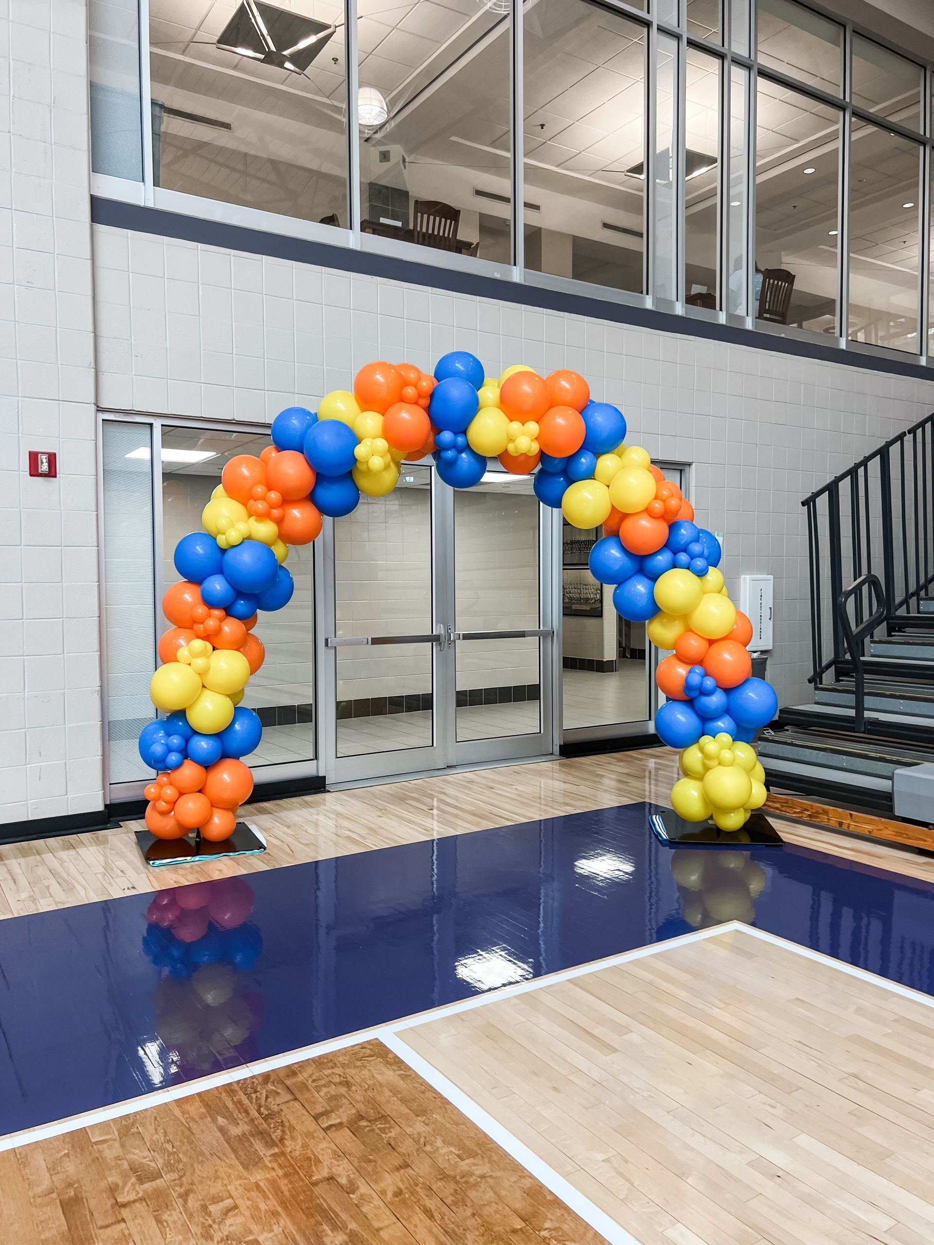 An organic balloon arch is sitting in front of a basketball court.