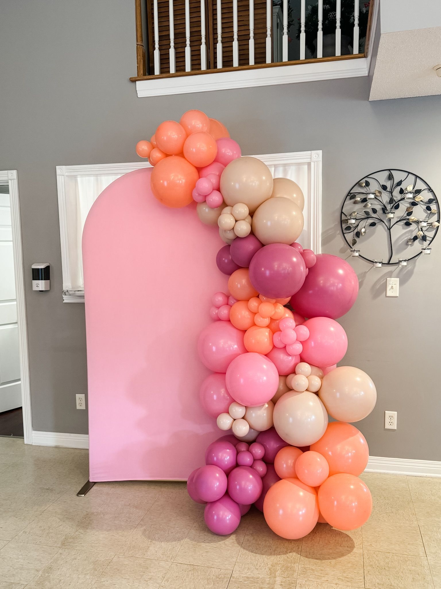 A bunch of pink and orange balloons are sitting on a wall in a room.