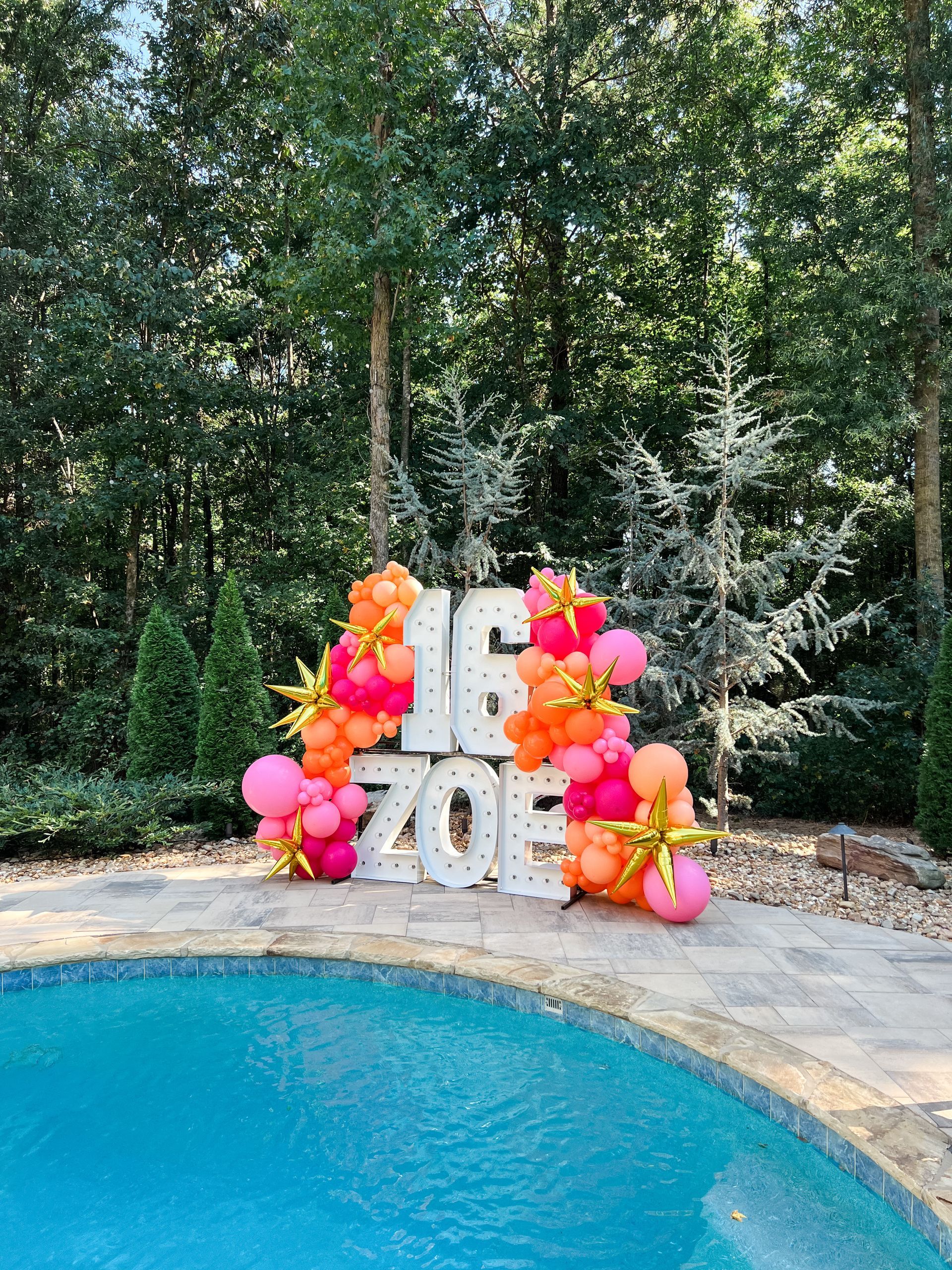 A swimming pool surrounded by balloons and a sign that says `` 16 zoe ''.