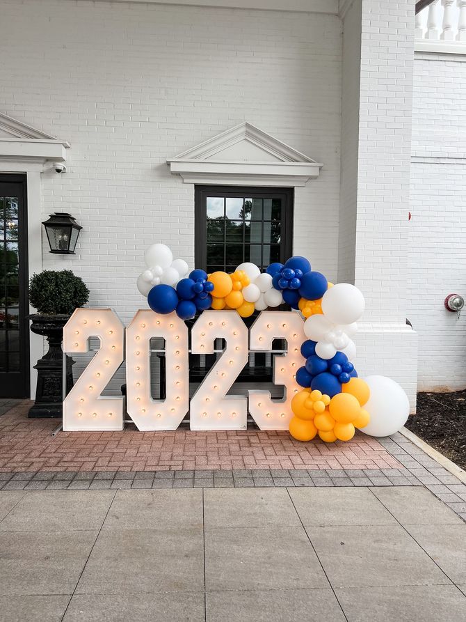a sign that says 2023 is surrounded by balloons in front of a white building