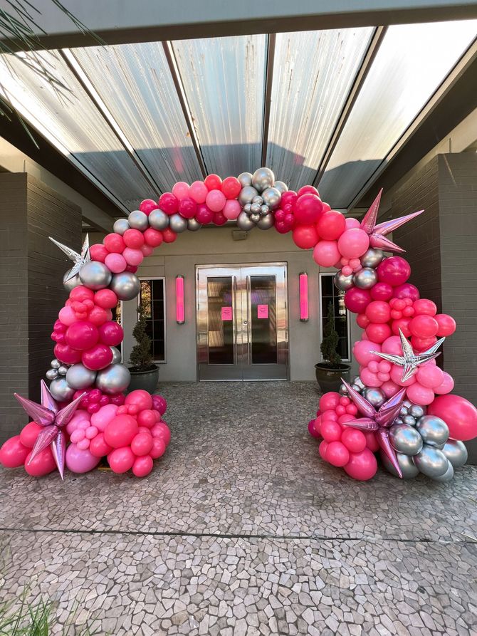 a pink and silver balloon arch is in front of a building