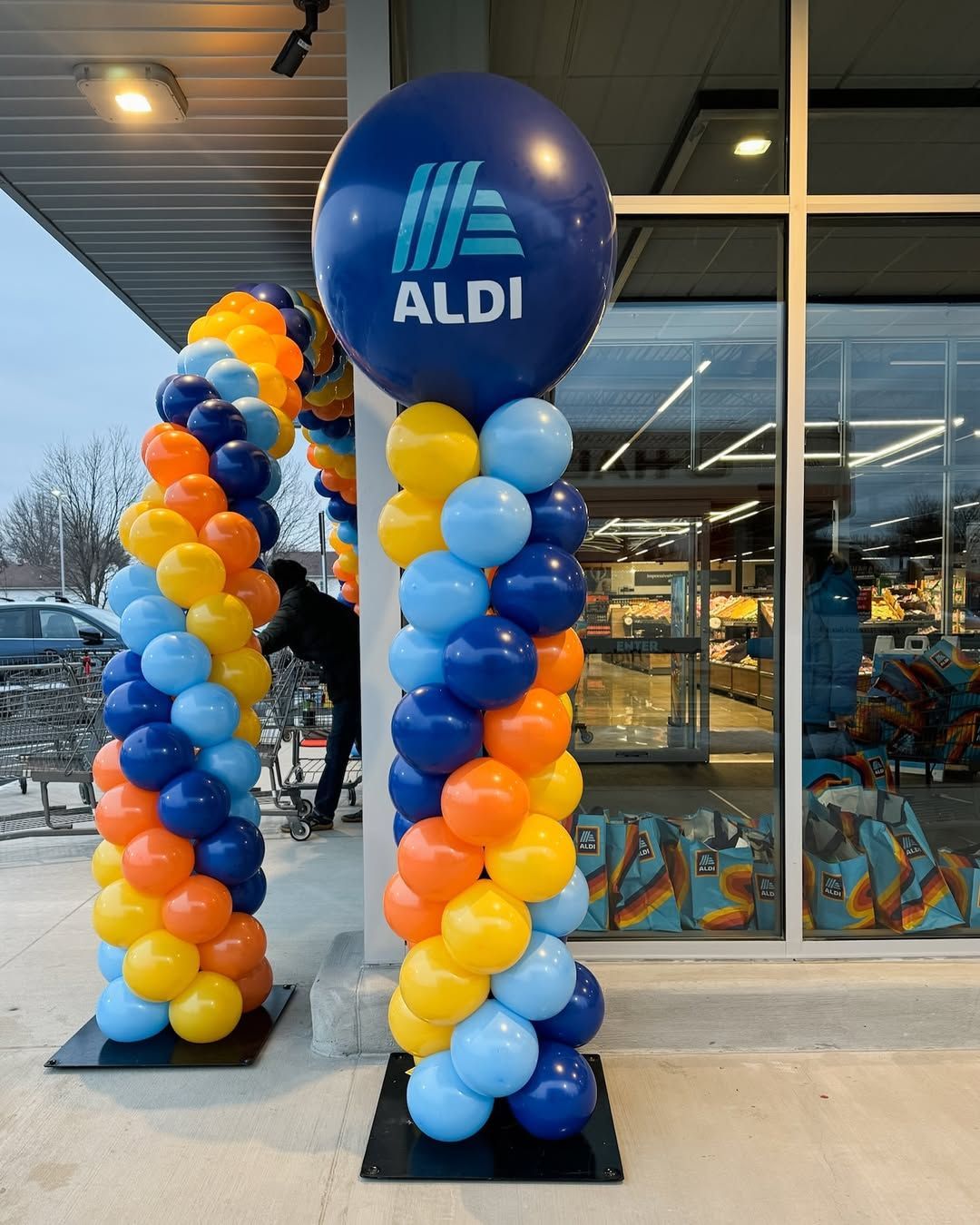 A balloon arch and column decorated in blue, yellow, and orange outside an Aldi store with a large logo balloon on top.