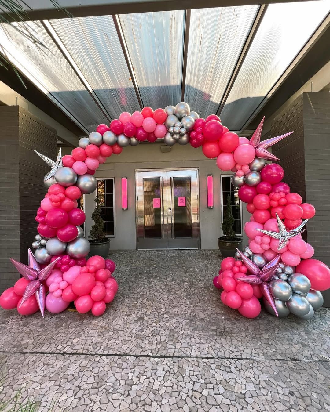 A festive arch made of pink and silver balloons framing a doorway, accented with star-shaped foil balloons.