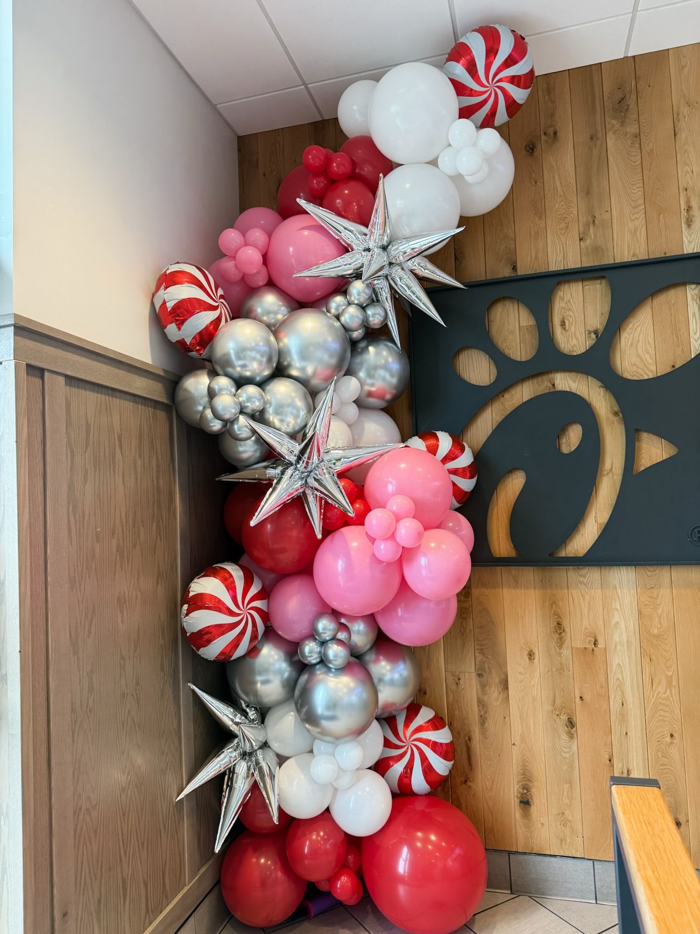 A festive Christmas balloon arch featuring red, white, silver, and pink balloons with star accents at a Chick-fil-A.