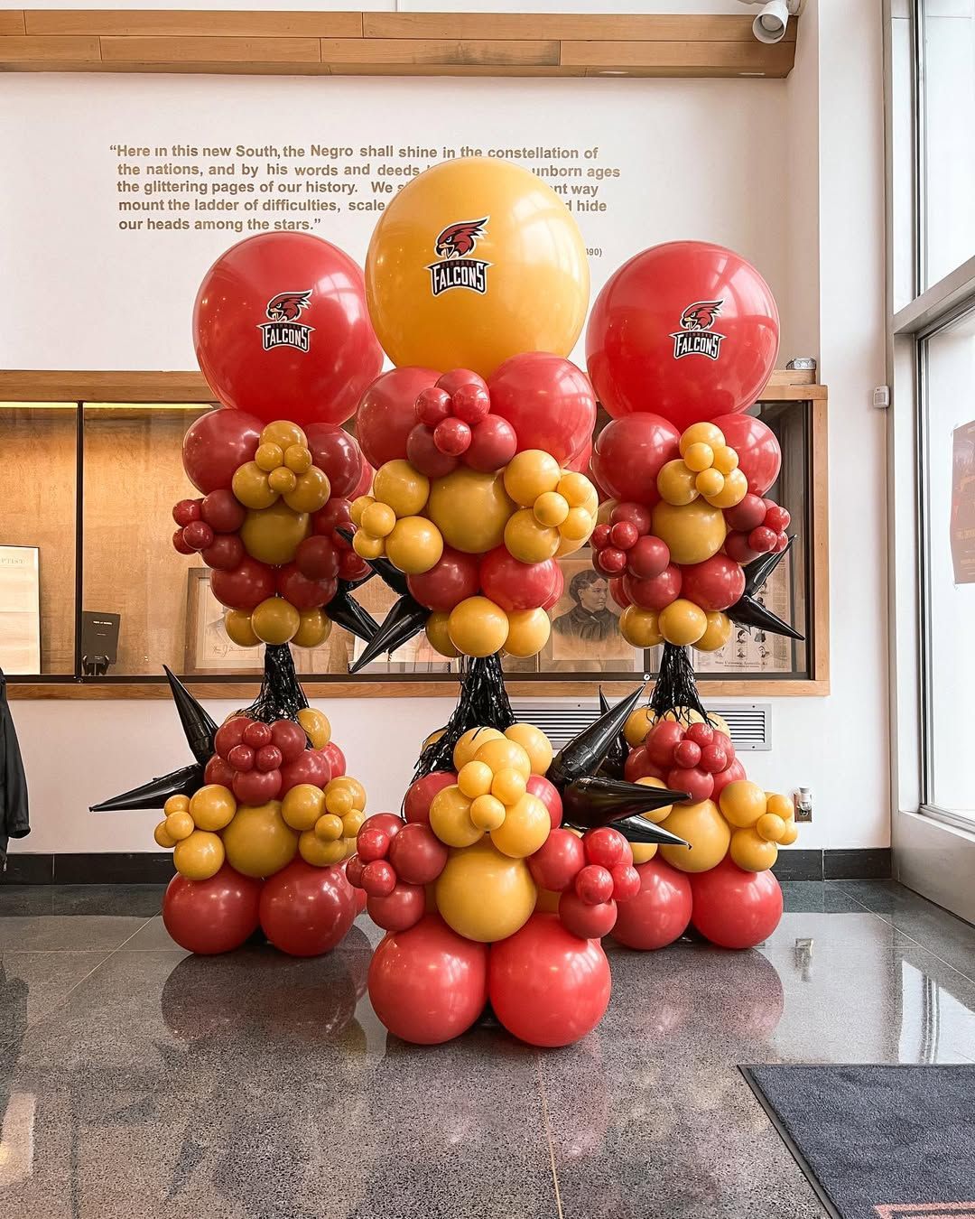 Three balloon pillars with red and yellow clusters, featuring large balloons with logos and black star-shaped accents.