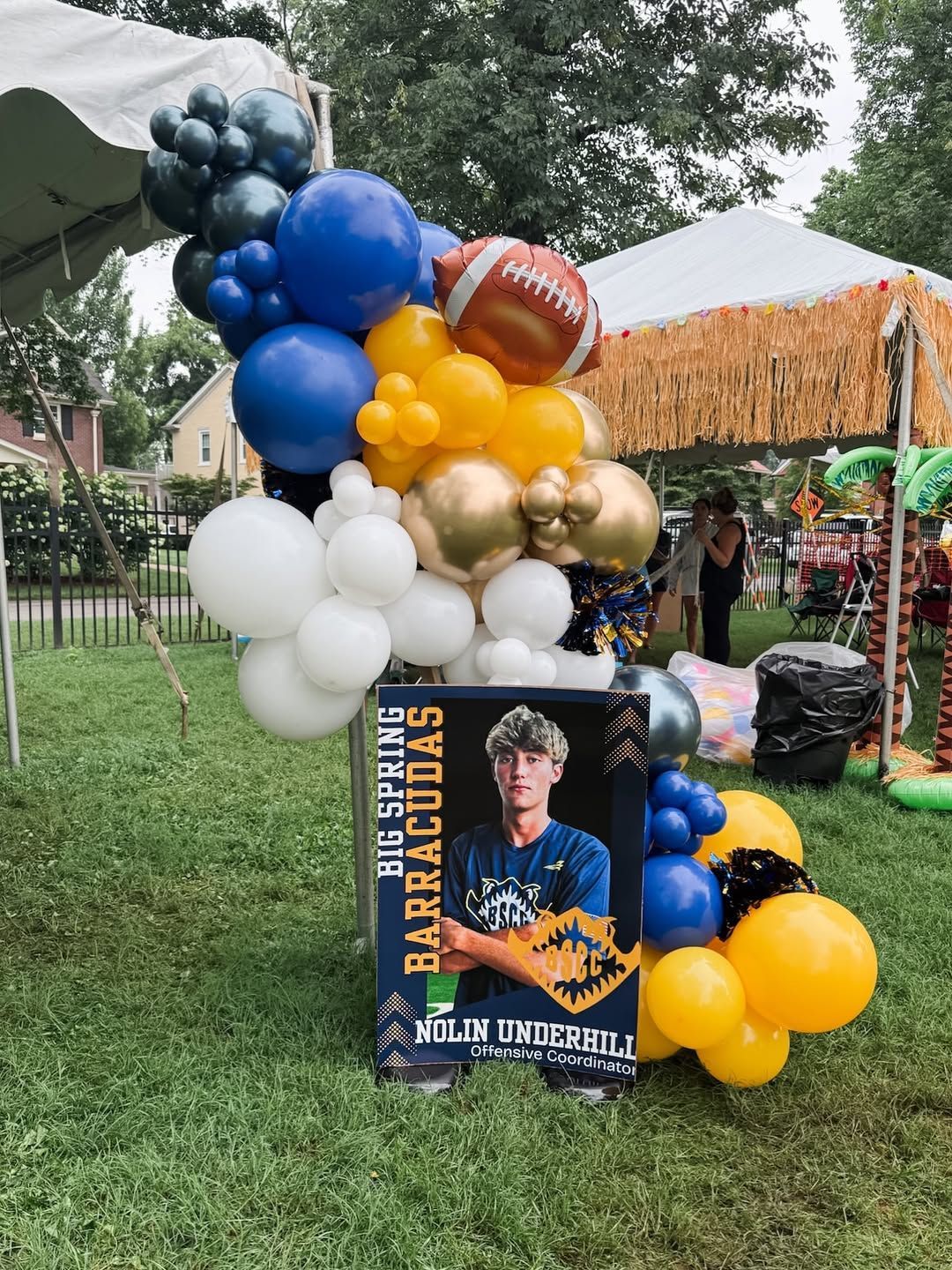 A commemorative sign for a Barracudas team member decorated with a large, colorful balloon arch outside.