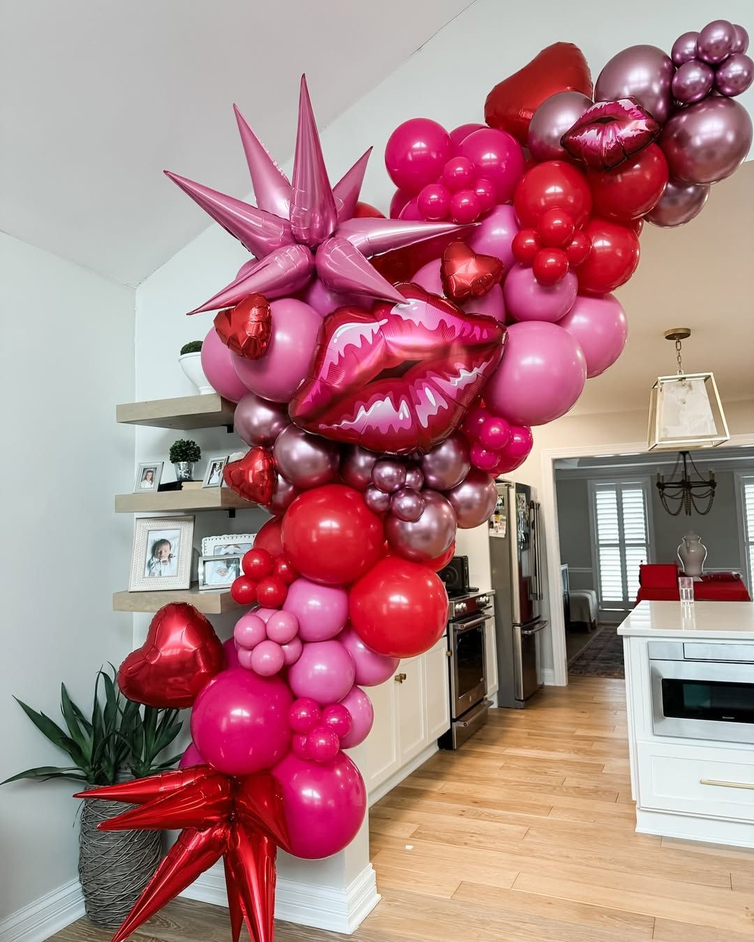 A balloon arch made of red, pink, and metallic spheres, featuring star-shaped foils and a large lips-shaped balloon.