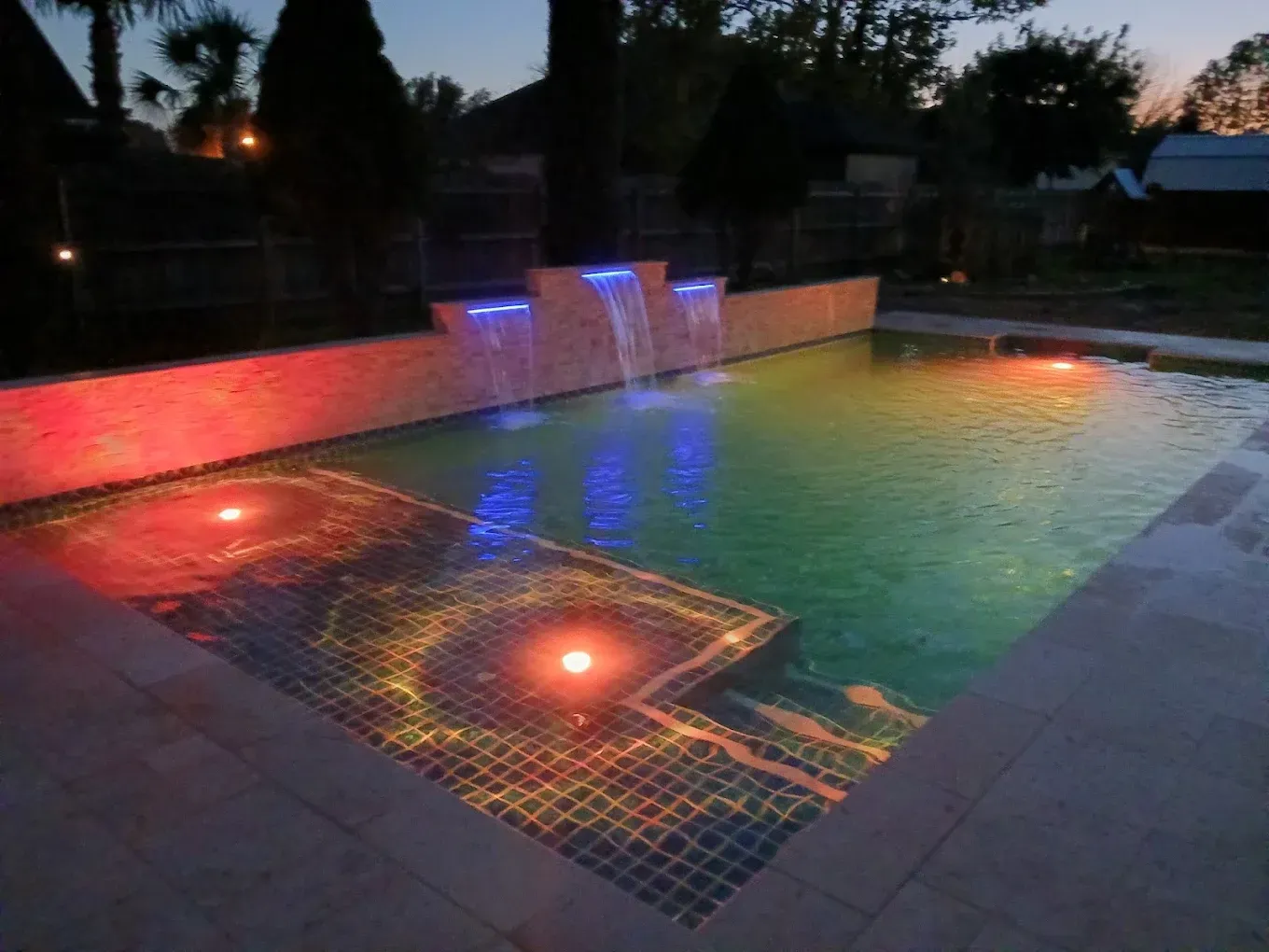A swimming pool with a waterfall and colored lights