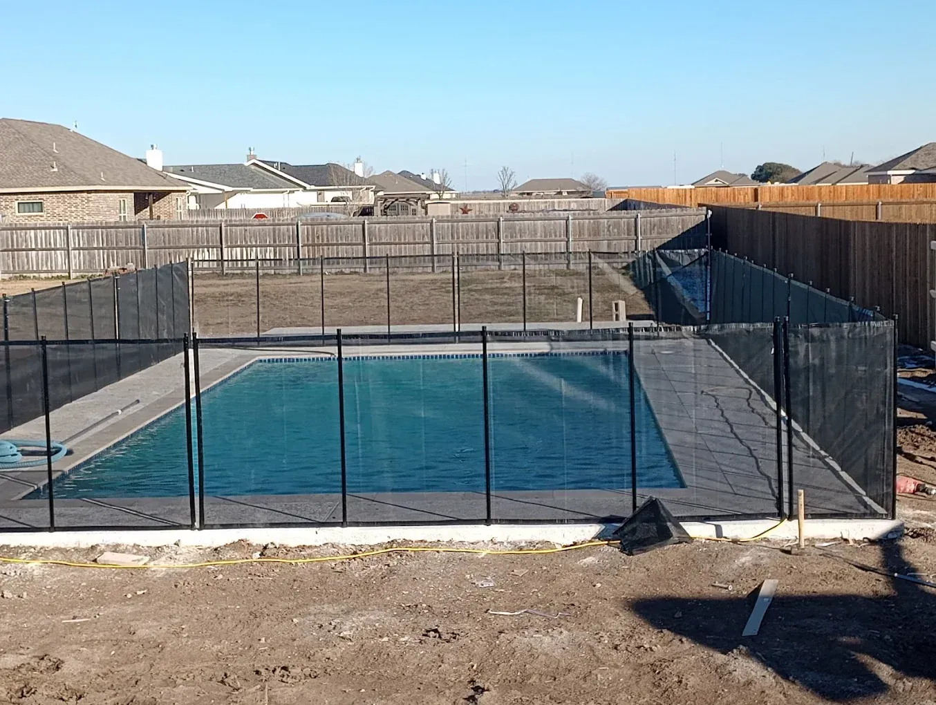 A fence surrounds a large swimming pool in a backyard.