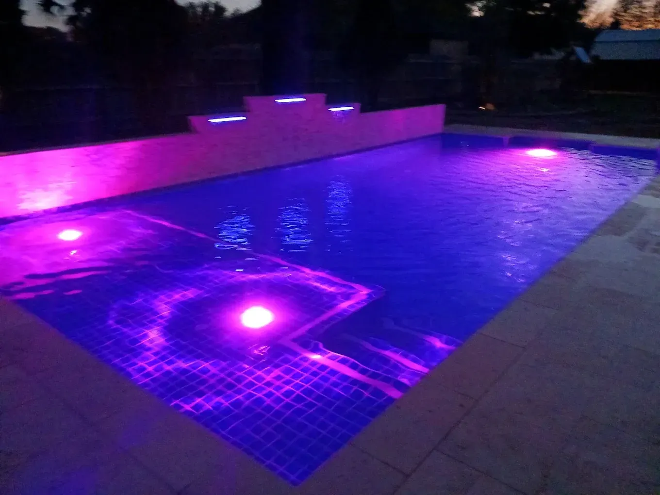 A large swimming pool is lit up with purple lights
