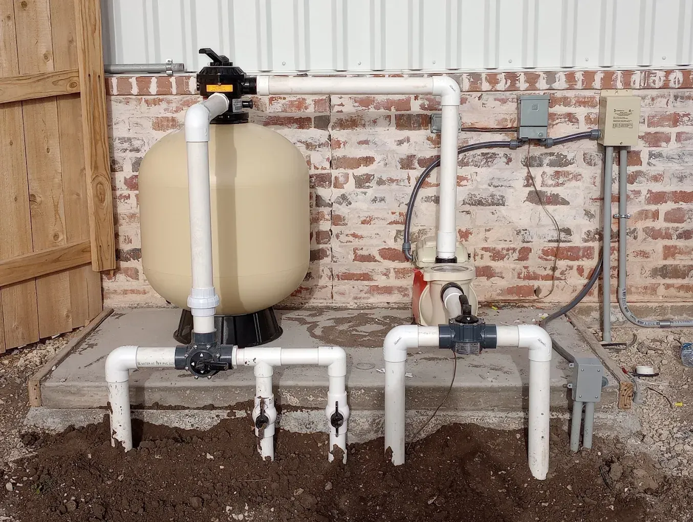 A swimming pool filter is sitting in the dirt next to a brick wall.