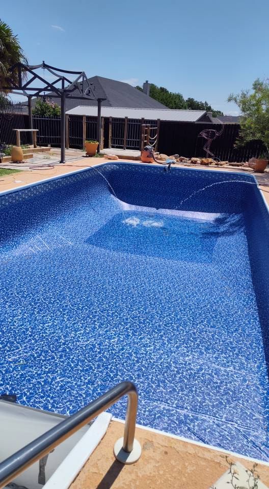 A large blue swimming pool with a house in the background
