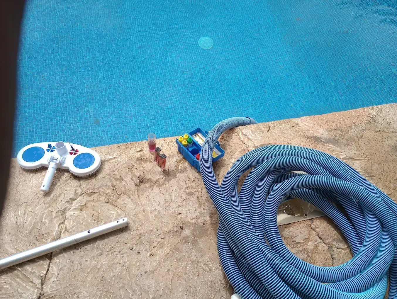 A hose and a vacuum cleaner are sitting on the edge of a swimming pool.