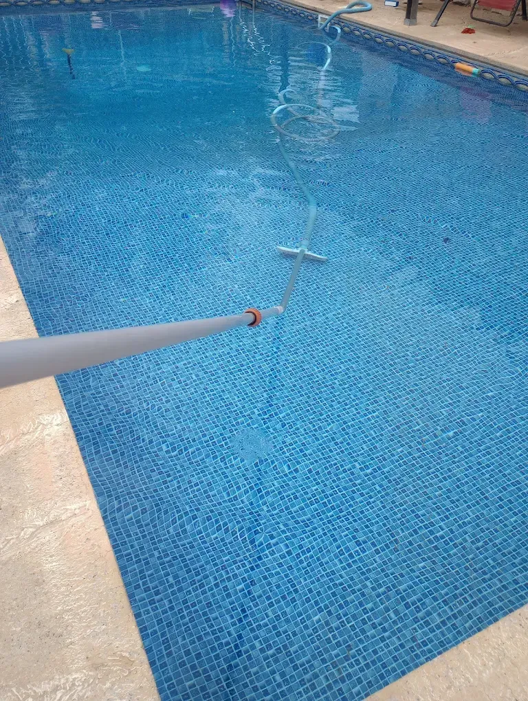 A person is cleaning a swimming pool with a vacuum cleaner.